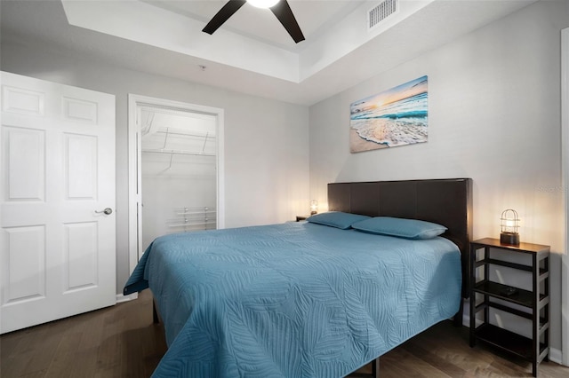 bedroom with a raised ceiling, wood finished floors, visible vents, and a closet