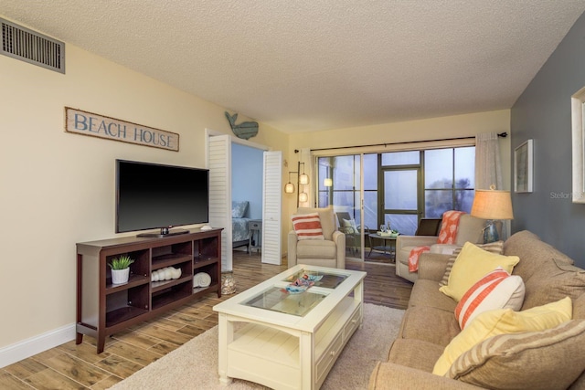 living room with wood finished floors, a textured ceiling, baseboards, and visible vents