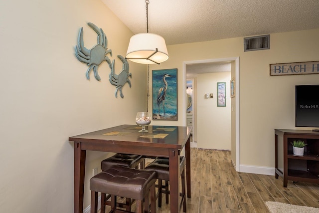 dining area with baseboards, a textured ceiling, visible vents, and wood finished floors