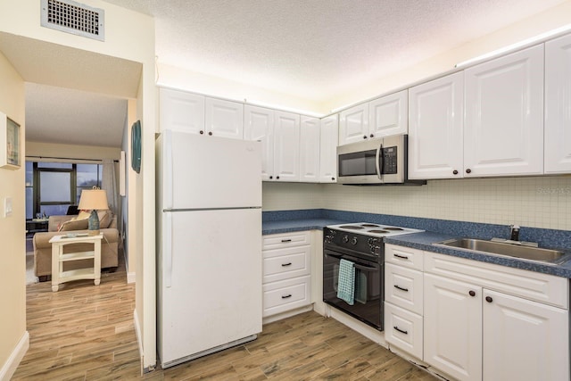 kitchen with stainless steel microwave, black / electric stove, a sink, visible vents, and freestanding refrigerator