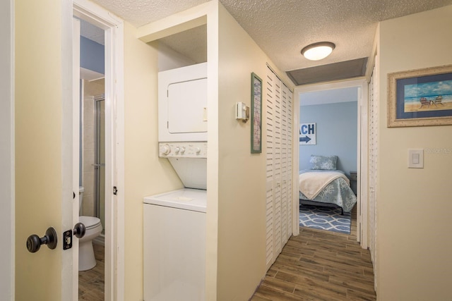 hall featuring dark wood-type flooring, a textured ceiling, and stacked washing maching and dryer