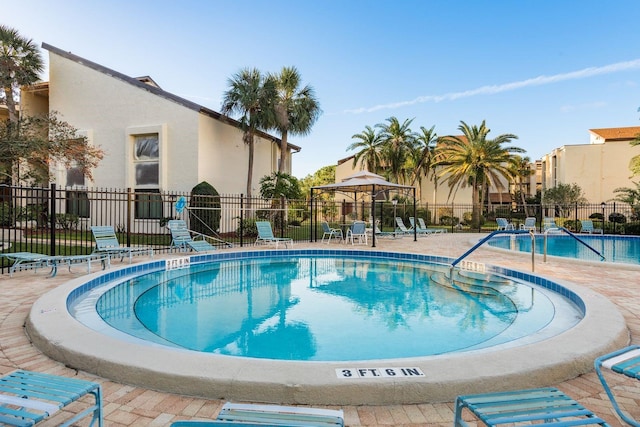 community pool with a gazebo, fence, and a patio area