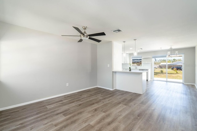unfurnished living room featuring visible vents, baseboards, wood finished floors, and ceiling fan with notable chandelier