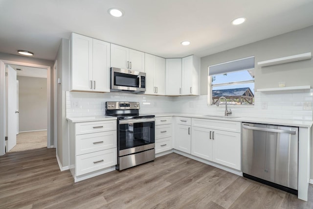 kitchen featuring open shelves, a sink, light countertops, white cabinets, and appliances with stainless steel finishes