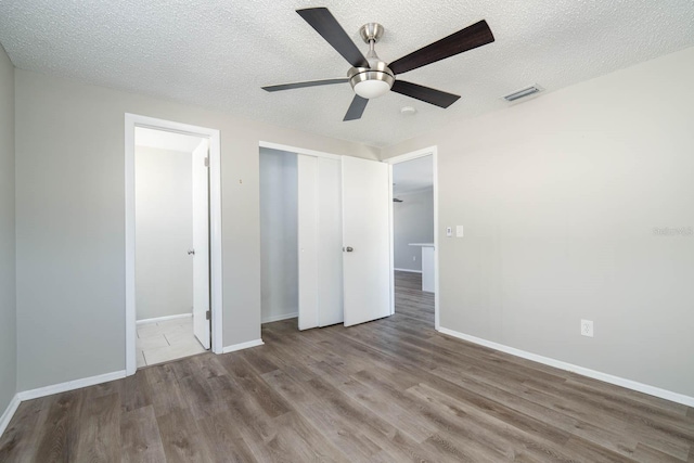 unfurnished bedroom featuring visible vents, baseboards, wood finished floors, a closet, and a textured ceiling