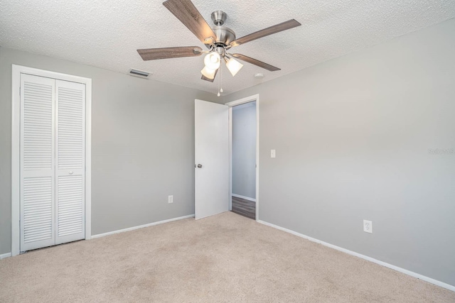 unfurnished bedroom featuring light carpet, visible vents, a textured ceiling, and a closet