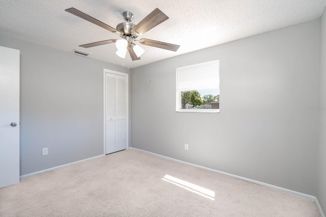 carpeted spare room featuring baseboards, visible vents, a textured ceiling, and a ceiling fan