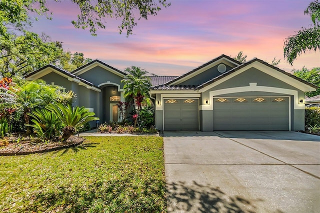 ranch-style home with a garage, stucco siding, a tile roof, driveway, and a yard