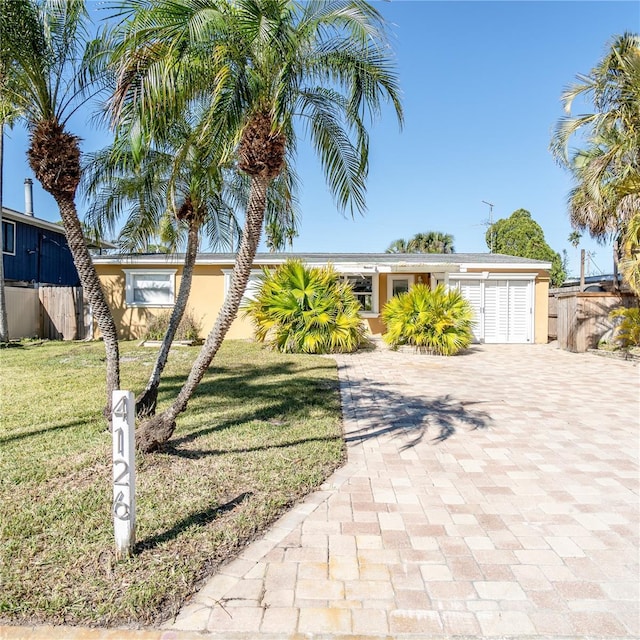 mid-century inspired home with stucco siding, decorative driveway, a front lawn, and fence