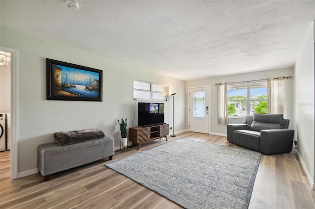 living room featuring a textured ceiling, washer / clothes dryer, baseboards, and wood finished floors