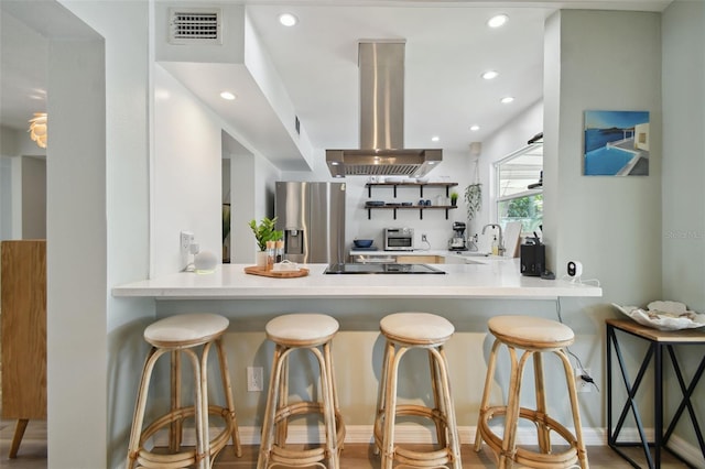 kitchen featuring visible vents, a peninsula, black electric cooktop, stainless steel fridge, and island range hood