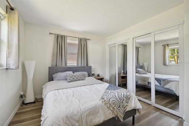 bedroom with two closets, baseboards, and wood finished floors