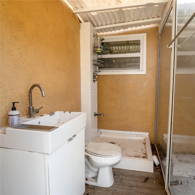 bathroom with a shower stall, toilet, a textured wall, wood finished floors, and vanity