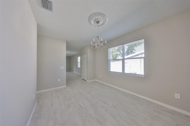 spare room with visible vents, light wood-style flooring, a textured ceiling, baseboards, and a chandelier