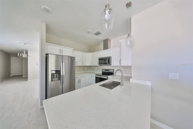 kitchen featuring visible vents, a peninsula, a sink, stainless steel appliances, and a notable chandelier