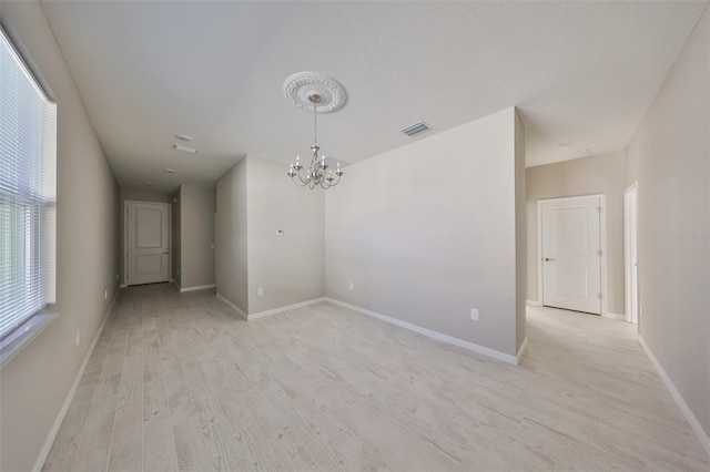 unfurnished room with light wood-type flooring, visible vents, baseboards, and an inviting chandelier