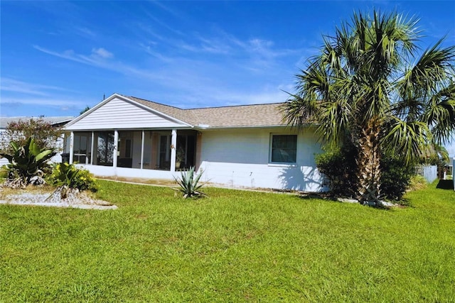 rear view of property with a yard, a sunroom, and a shingled roof