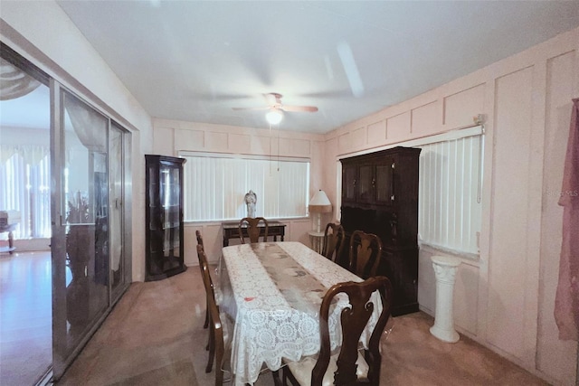 dining space with a decorative wall, light carpet, and ceiling fan