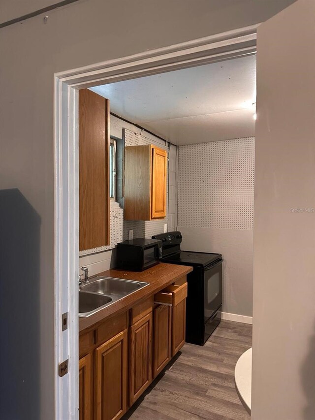 5562 S US-301, Bushnell, FL 33513 - kitchen featuring baseboards, a sink, black appliances, light wood-style floors, and brown cabinets