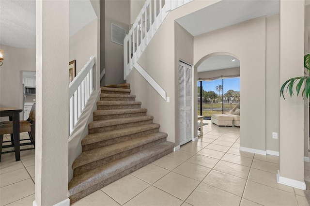 stairway with arched walkways, tile patterned floors, a high ceiling, and baseboards