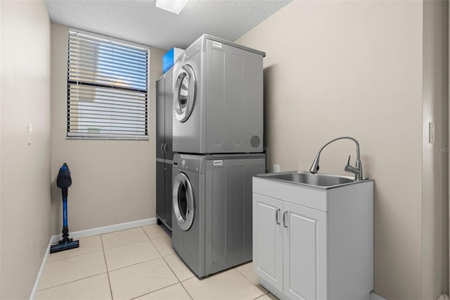 washroom featuring a sink, a textured ceiling, cabinet space, light tile patterned flooring, and stacked washer / dryer