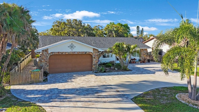 view of front of home featuring stone siding, an attached garage, fence, and decorative driveway