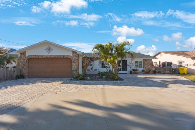 ranch-style house featuring fence, stone siding, decorative driveway, stucco siding, and an attached garage