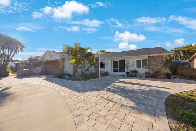 single story home featuring decorative driveway, fence, stone siding, and a garage