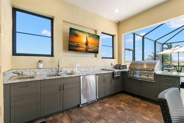 kitchen featuring freestanding refrigerator, a sink, brick floor, and gray cabinetry