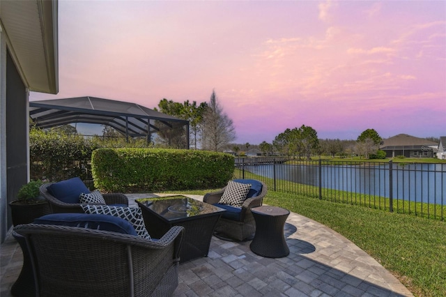 patio terrace at dusk featuring glass enclosure, a water view, a lawn, and a fenced backyard