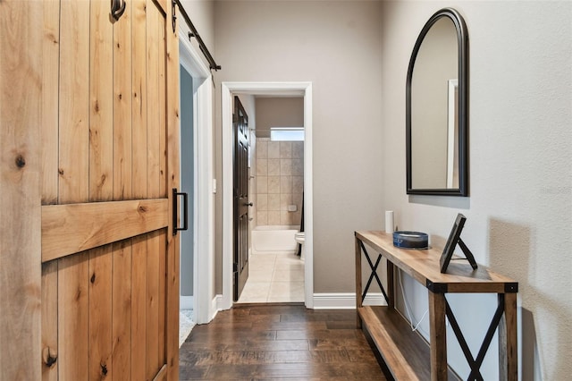 hallway featuring baseboards, a barn door, and wood finished floors
