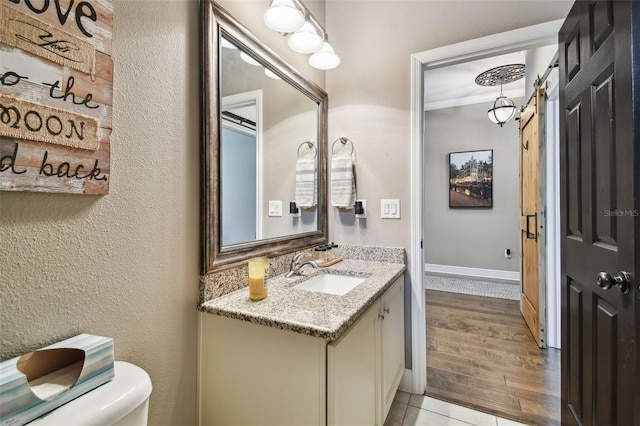 bathroom featuring baseboards, toilet, ornamental molding, wood finished floors, and vanity