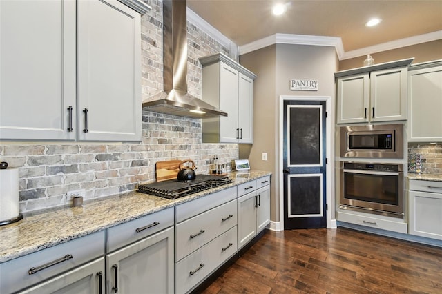 kitchen with backsplash, appliances with stainless steel finishes, wall chimney exhaust hood, crown molding, and dark wood-style flooring