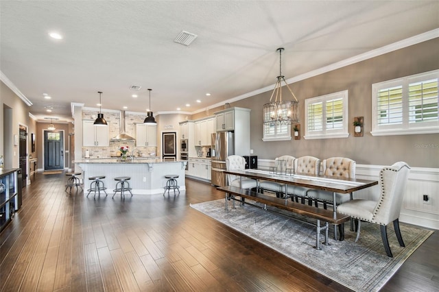 dining area with a wainscoted wall, visible vents, dark wood-style floors, and crown molding