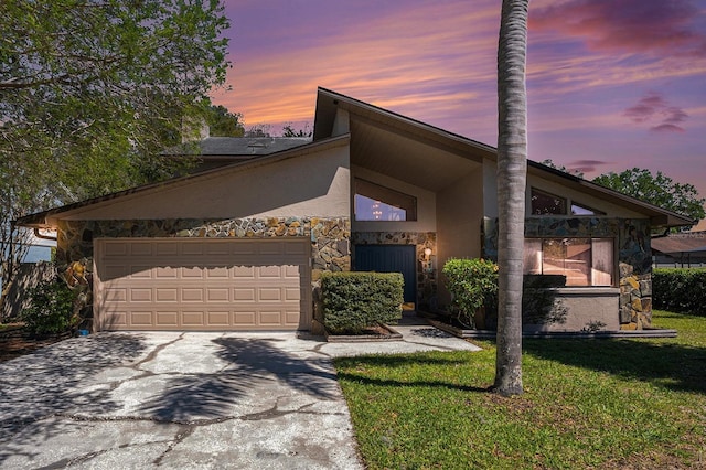 mid-century home with concrete driveway, stucco siding, a lawn, a garage, and stone siding