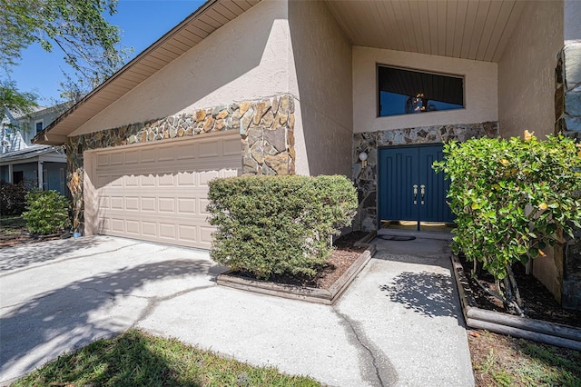 property entrance with stone siding, stucco siding, an attached garage, and concrete driveway