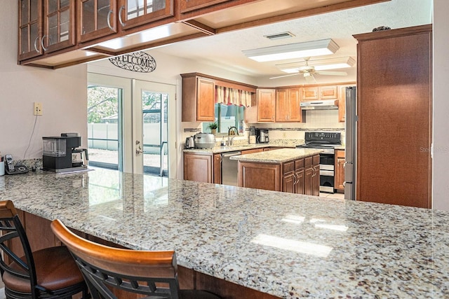 kitchen featuring light stone counters, visible vents, a peninsula, stainless steel appliances, and under cabinet range hood