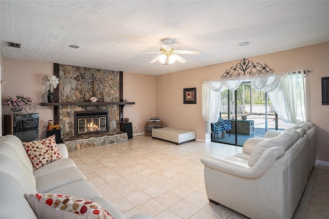 living room with a stone fireplace, a textured ceiling, visible vents, and ceiling fan