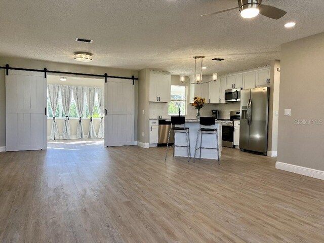 kitchen featuring open floor plan, ceiling fan, stainless steel appliances, and a barn door