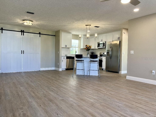 kitchen featuring a barn door, light wood-style flooring, open floor plan, and appliances with stainless steel finishes