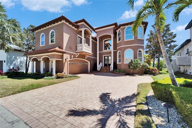 mediterranean / spanish house with a tile roof, a garage, a balcony, stucco siding, and decorative driveway