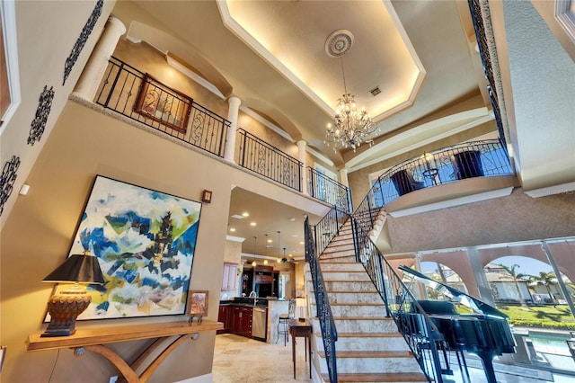 staircase with a healthy amount of sunlight, a towering ceiling, ornate columns, and an inviting chandelier