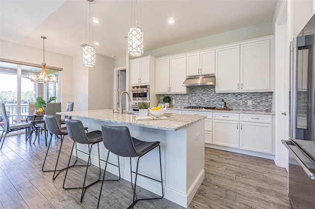 16 Franklin Ct S Unit A, Saint Petersburg, FL 33711 - kitchen featuring under cabinet range hood, a center island with sink, decorative backsplash, and light wood-style flooring