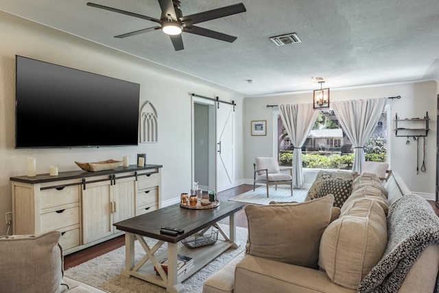 1828 Stancel Dr, Clearwater, FL 33764 - living room with visible vents, dark wood-type flooring, ceiling fan with notable chandelier, a textured ceiling, and a barn door