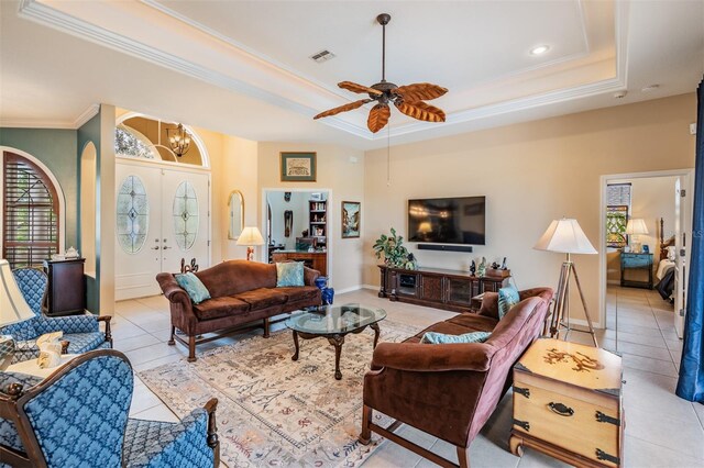 living room with crown molding, a ceiling fan, a raised ceiling, light tile patterned floors, and visible vents