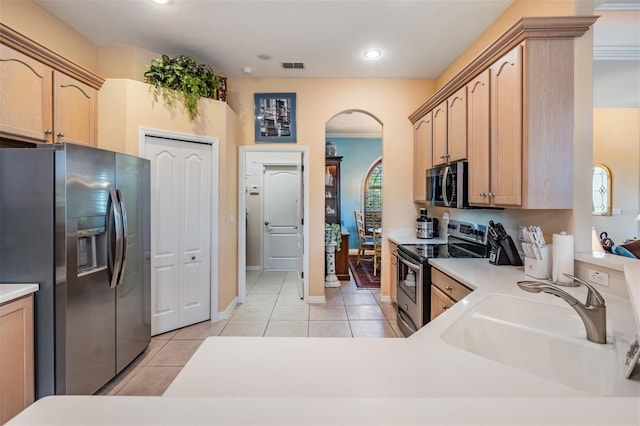 kitchen featuring a sink, light brown cabinetry, stainless steel appliances, visible vents, and arched walkways
