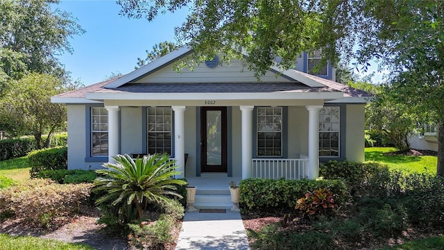 bungalow featuring a porch, stucco siding, and a shingled roof