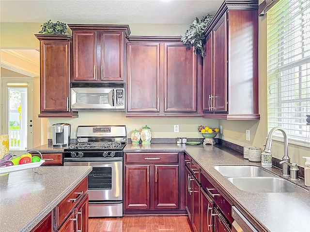 kitchen featuring stainless steel appliances, a sink, reddish brown cabinets, and dark countertops