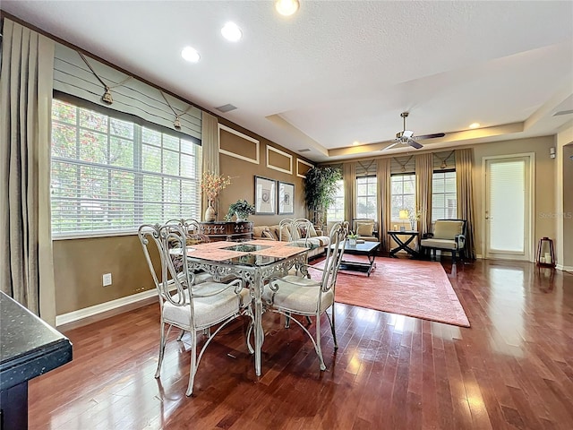 dining space featuring baseboards, hardwood / wood-style flooring, a tray ceiling, and ceiling fan