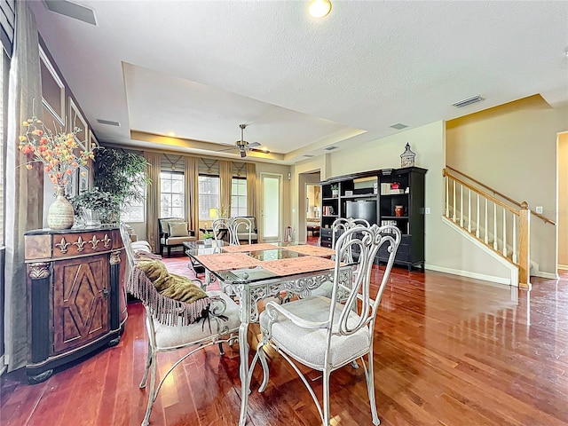 dining room with stairs, wood finished floors, ceiling fan, a tray ceiling, and baseboards
